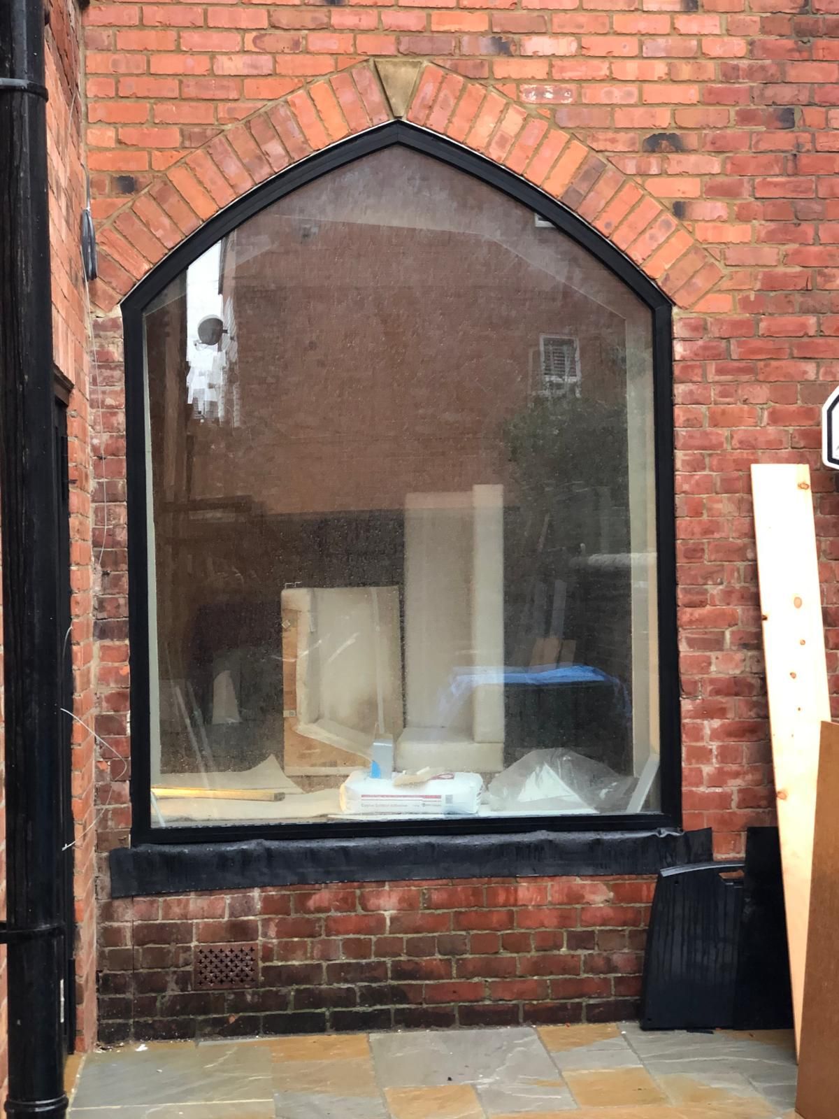 Tall arched window with a red-brick soldier-course head set into an exposed brick wall over a sandstone-paved courtyard