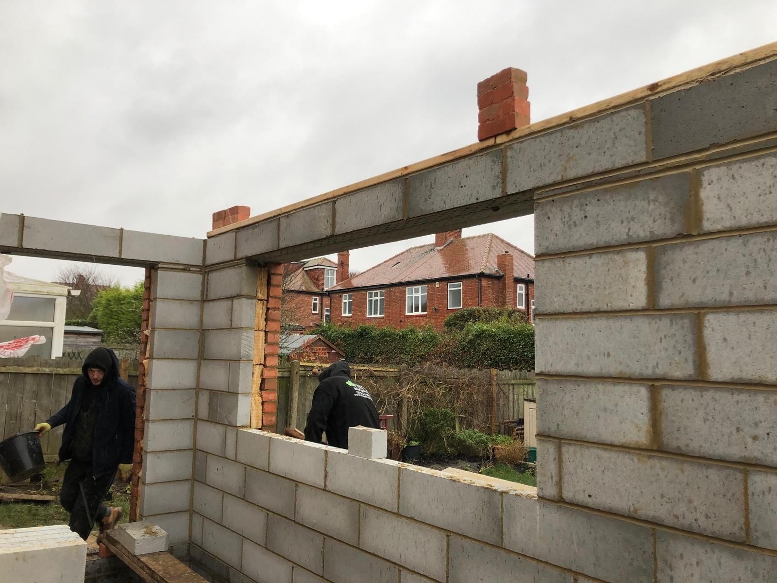 Low red-brick boundary wall with sandstone copings, brick piers and black metal railings along a paved footpath