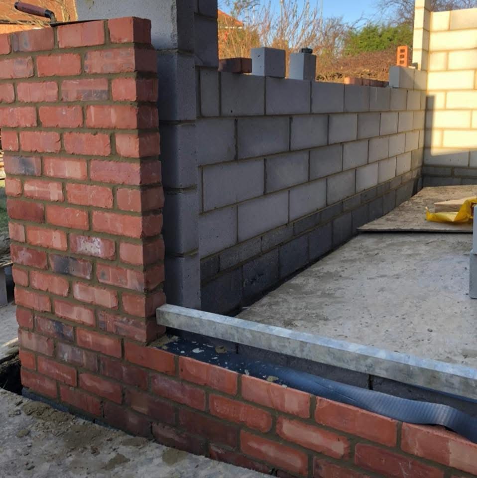 New brick-faced and block cavity wall with a red-brick return pier and damp-proof course at footing level