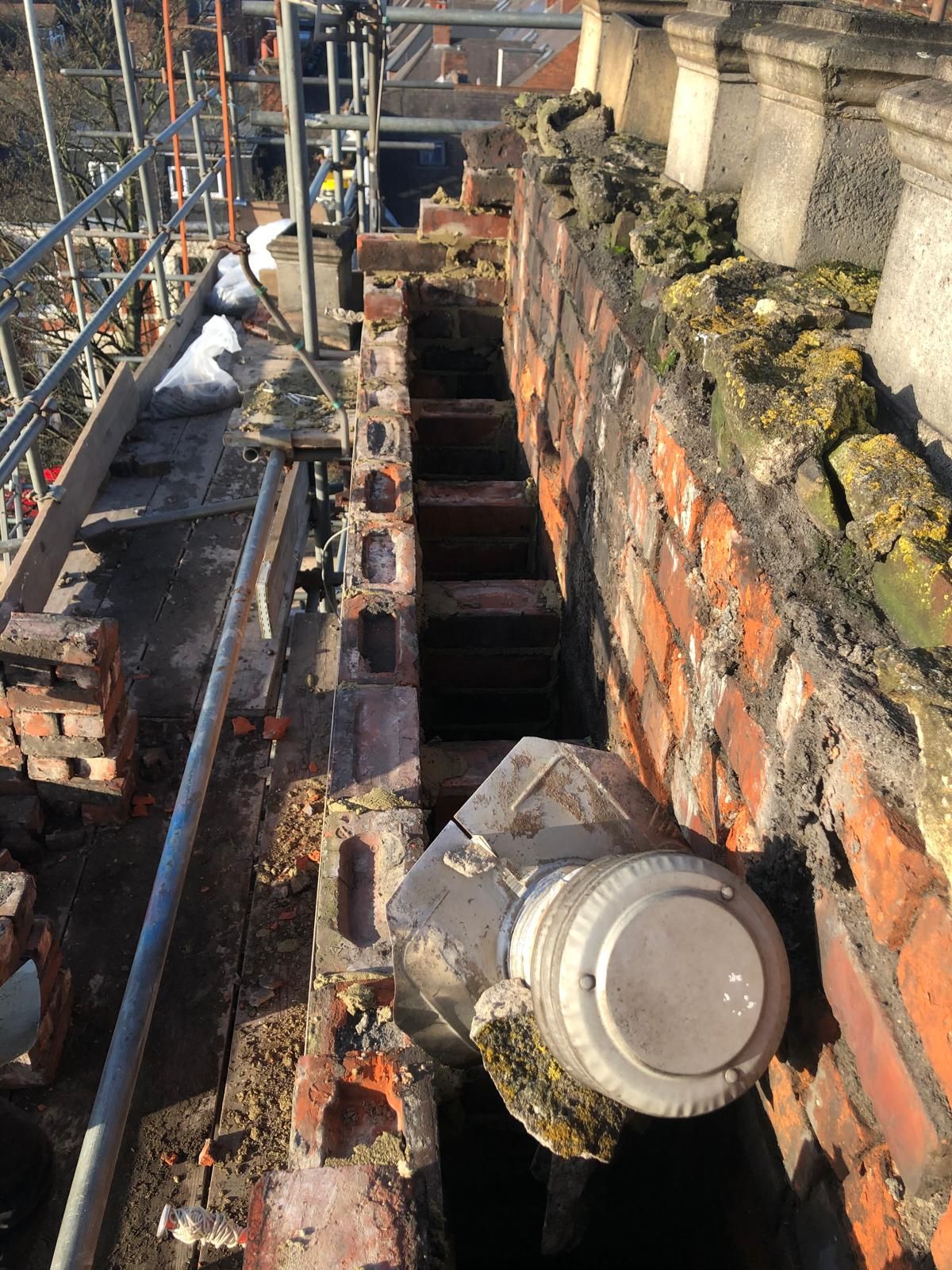 Weathered, blackened chimney brickwork with eroded mortar on scaffolding before rebuilding