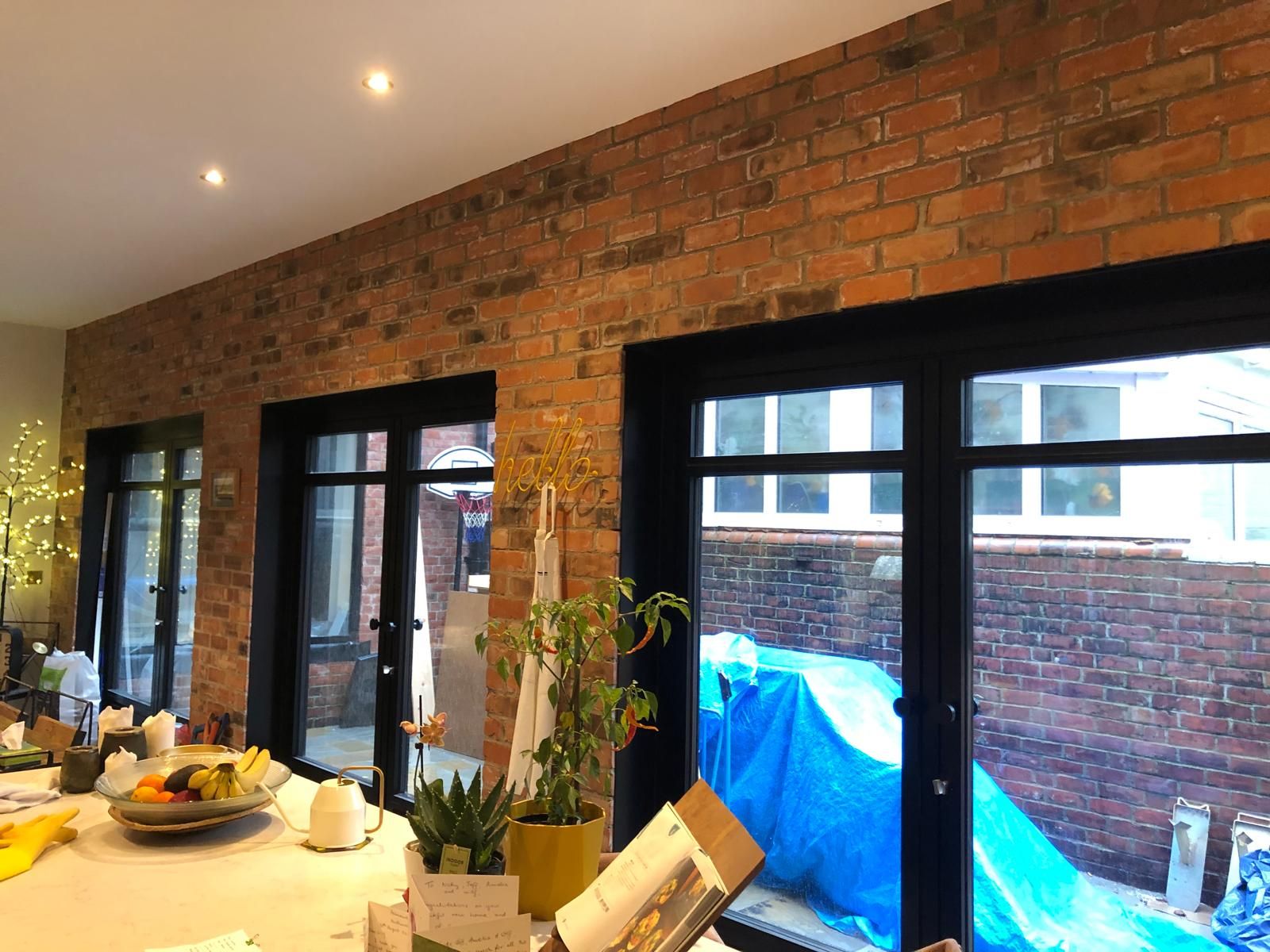 Kitchen-diner with an exposed red-brick wall, three sets of black-framed glazed doors, recessed downlights and a marble island in the foreground