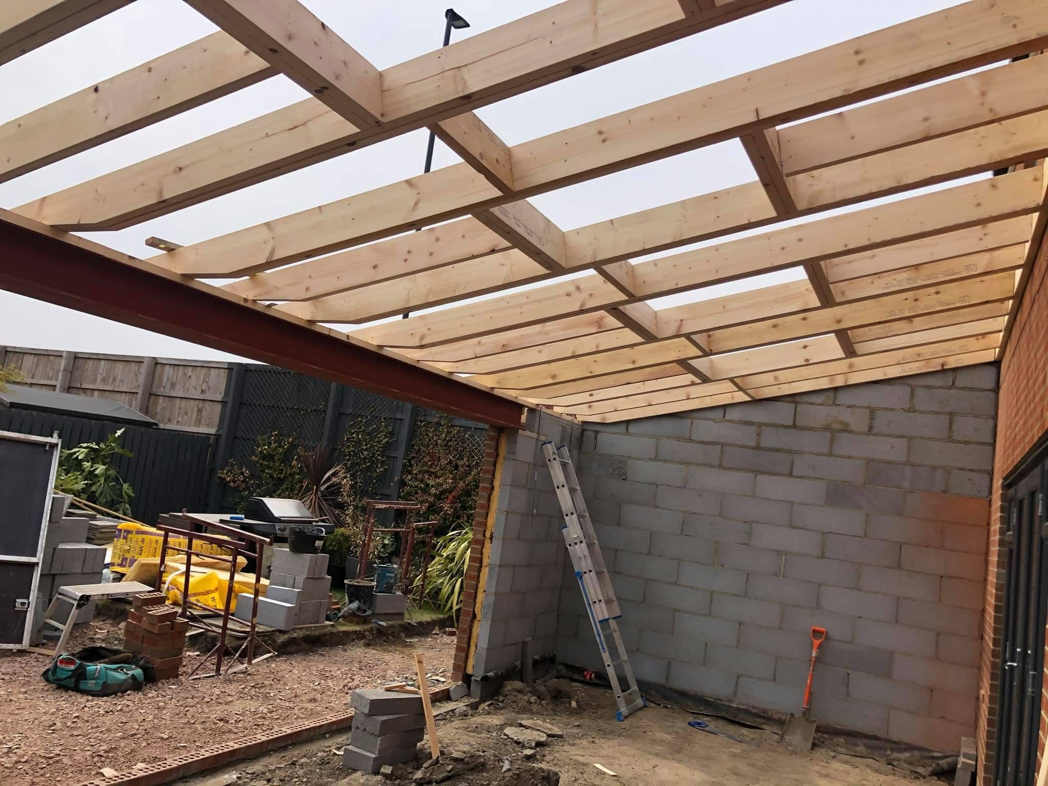 New timber flat-roof joists spanning onto fresh blockwork with the existing fence and garden behind