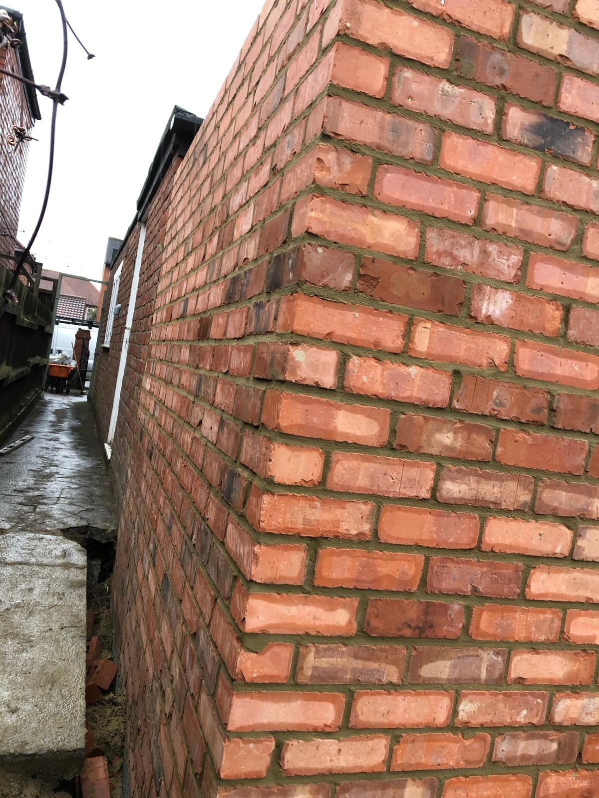 New red-brick front garden wall with a moulded sandstone pier cap and black railings, a red sports car on the drive behind