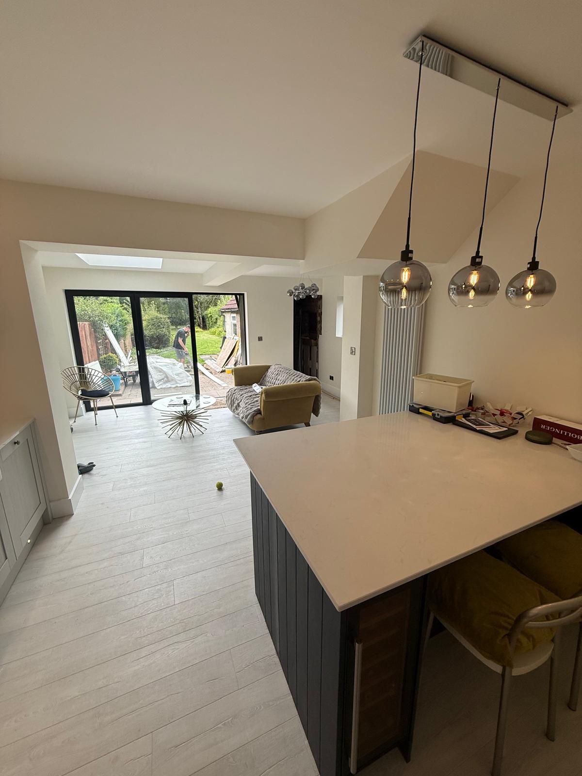 Grey shaker kitchen-diner with navy island and bar stools looking through bifold doors to the garden, three smoked-glass pendants overhead