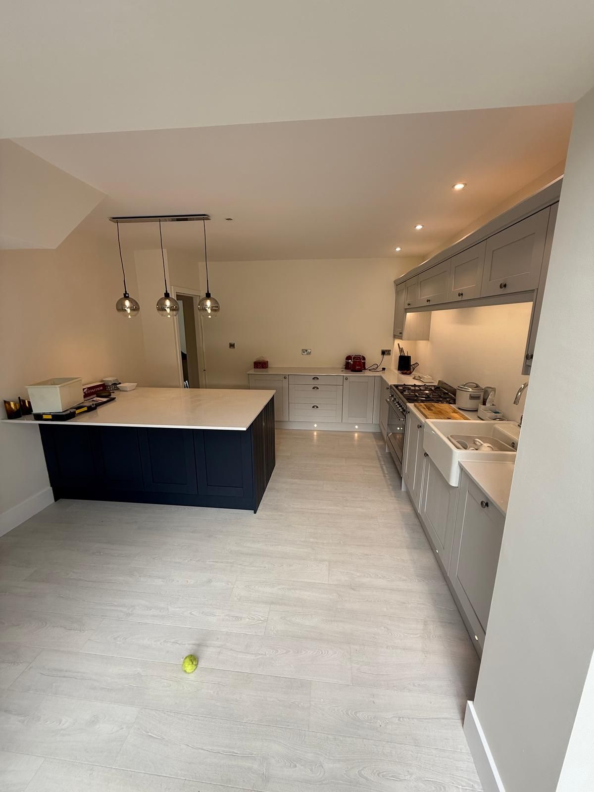 Grey shaker kitchen with a navy island, white quartz worktops, range cooker, twin Belfast sinks and globe pendant lights over light wood flooring