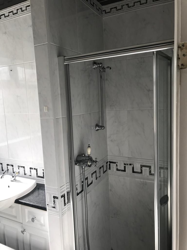 Loft en-suite with a sloped ceiling, black-framed walk-in shower screen, slate tray, gloss-black vanity and backlit mirror