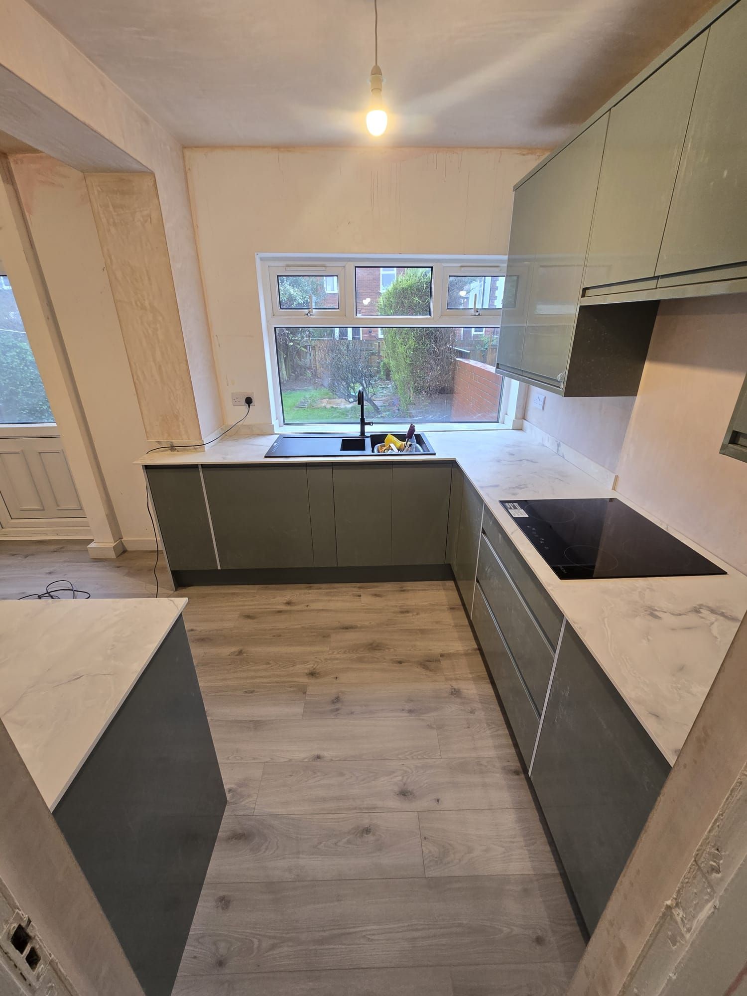 A sage-green handleless kitchen with marble worktops, fitted by NEBS