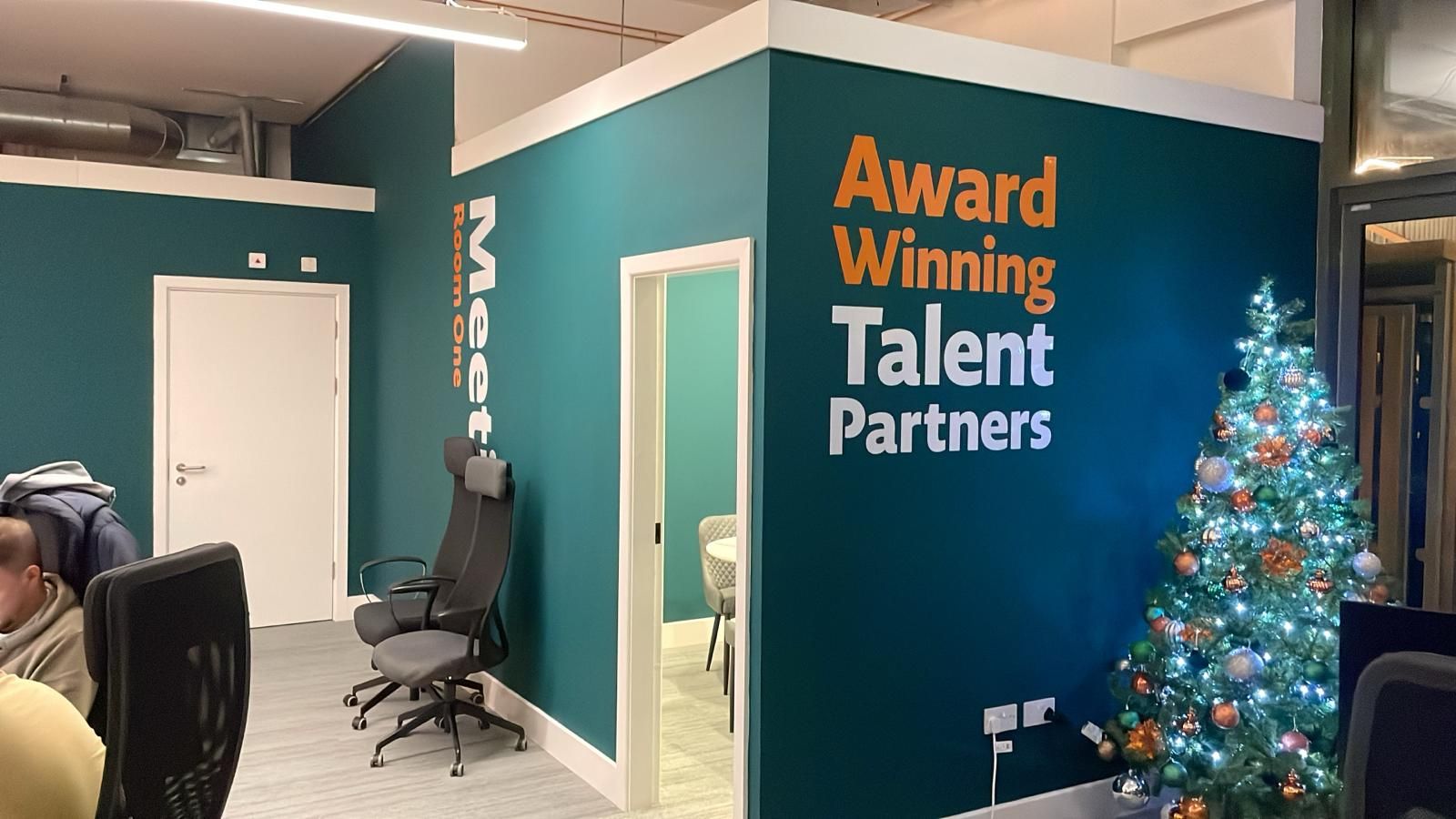 Teal feature wall with white and orange "Award Winning Talent Partners" branded graphics beside a white meeting-room door