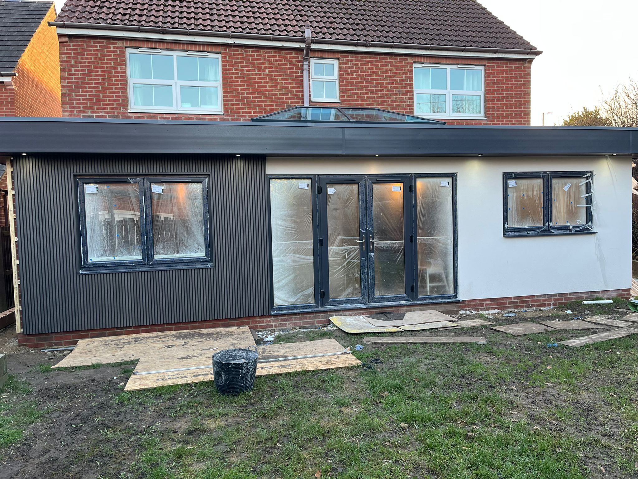 Close view of the finished extension showing the bifold doors, white-rendered end panel and lantern roof at dusk