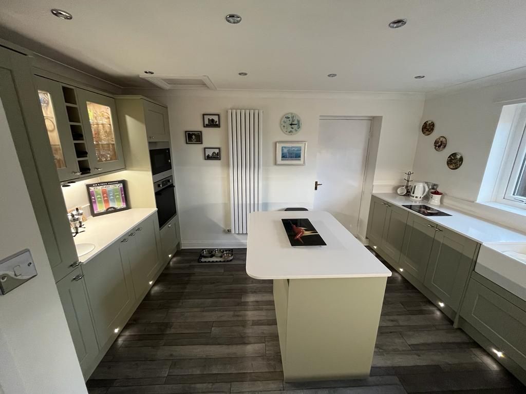Olive-green shaker kitchen with white worktops, a curved island, vertical column radiator and decorative plates on the wall