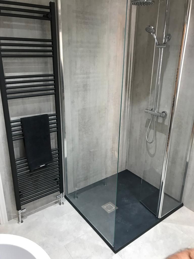 Walk-in shower with a slate-grey tray, glass screen, concrete-effect tiling and a tall black ladder towel radiator