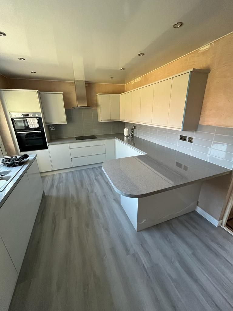 White handleless kitchen with grey speckled worktops, chimney extractor and curved breakfast-bar end on grey wood-effect flooring